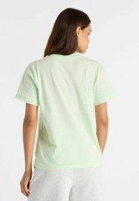 Camiseta de algodón verde claro con mangas cortas y cuello redondo. Textura suave, corte relajado, sin patrones ni gráficos visibles.
