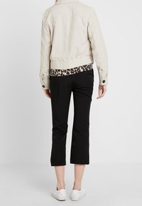 Beżowa lniana kurtka o skróconym fasonie, w zestawieniu z czarnymi spodniami o skróconej długości i białymi trampkami. Zauważalny detal w panterkę na krawędzi kurtki.