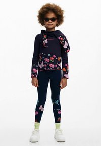 Granatowa bluzka z długim rękawem z wzorami kwiatów i motyli, połączona z granatowymi legginsami ozdobionymi kolorowymi napisami i wzorami. Na nogach białe trampki.