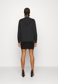 Czarny longsleeve z teksturowanym wzorem w zygzak na plecach, w połączeniu z dopasowaną czarną spódnicą i czarnymi sandałami na obcasie.