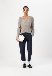 Beiger Strickpullover, lockere Passform, mit weitem Ausschnitt. Navyblaue hochgeschnittene Hose, weiße Socken, schwarze Mokassins und eine kleine weiße Handtasche.