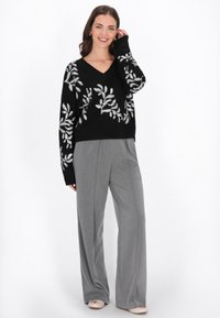 Czarny sweter dzianinowy z dekoltem w kształcie litery V i haftem w srebrne liście. Szare spodnie o szerokich nogawkach. Różowe baleriny. Gładkie białe tło.