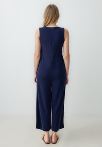 Tuta senza maniche blu navy con design a gamba dritta, caratterizzata da una chiusura lampo sul retro e una texture di tessuto liscia.