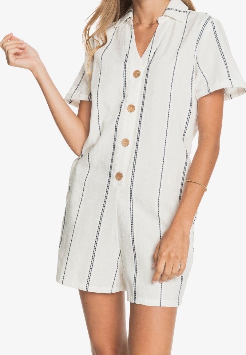 Combinaison courte blanche à manches courtes avec des rayures verticales bleu marine, fermeture à boutons sur le devant, col, coupe décontractée et boutons en bois naturel. Tissu doux et texturé.