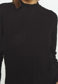 Czarny sweter z golfem, prążkowany, z długimi rękawami, wyróżniający się fakturowanym materiałem i dopasowanym krojem.