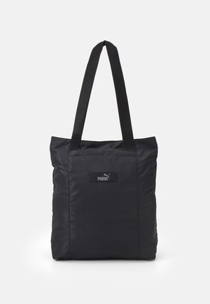 Saco em nylon preto com alças curtas e resistentes; apresenta uma superfície texturizada e um pequeno emblema na frente. Design simples e quadrado.