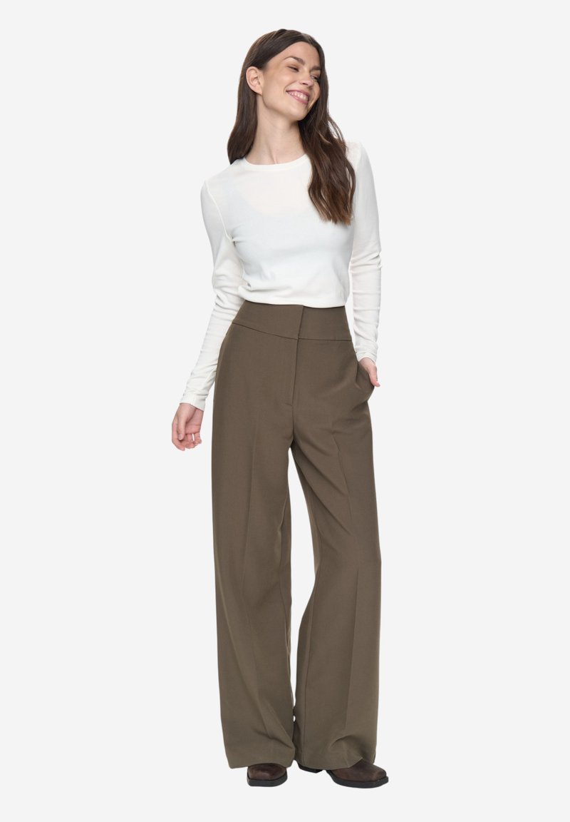 Pantalon large vert olive à taille haute, assorti à un haut blanc ajusté à manches longues. Tissu lisse et design structuré.