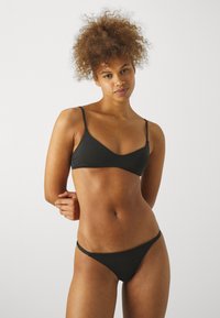 Black bikini set featuring a v-neck bralette with thin straps and a low-rise bikini bottom. Made of smooth fabric with minimal detailing.