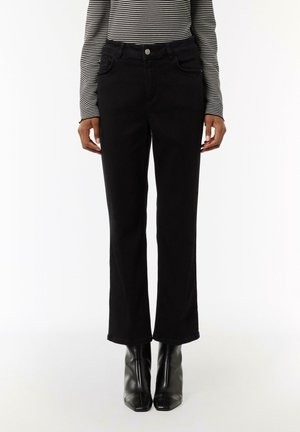 Black denim flared jeans with front pockets, a button closure, and a smooth texture. Worn with black high-heeled boots.