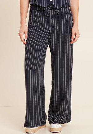 Marineblaue, weit geschnittene Hose mit weißen vertikalen Nadelstreifen, Tunnelzug am Bund, getragen mit weißen Plateau-Sneakern.