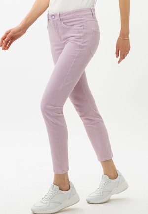 Woman wearing pastel pink slim-fit jeans and white sneakers, walking with arms relaxed at sides.