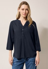 Marineblaue Bluse mit langen Ärmeln und V-Ausschnitt, drei Knöpfen vorne und elastischen Ärmelbündchen, aus weichem, glattem Stoff.