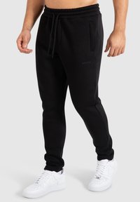 Schwarze Sweatpants aus weichem Stoff, mit elastischem Bund und Tunnelzug, seitlichen Taschen, gerippten Bündchen und einem dezenten Logo auf dem Oberschenkel.
