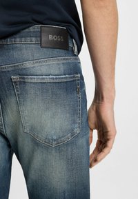 Jeans in denim blu scuro con una finitura sbiadita, dotati di tasche posteriori e di un'etichetta in pelle con la scritta "BOSS" nella parte superiore.