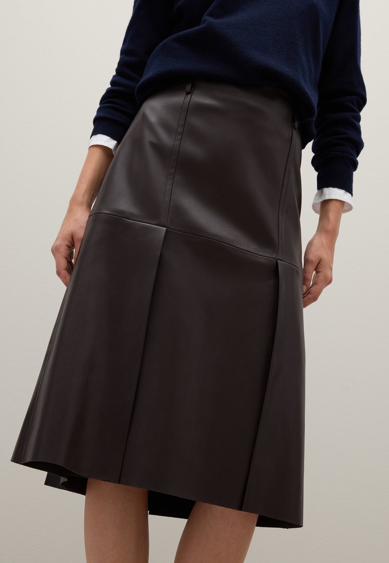 Bruine leren midi-rok met plooien aan de zoom, met een gladde textuur en een aangesloten taille. Gestyled met een marineblauwe trui.