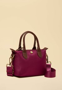 Väike ristkülikukujuline burgundiapunane käekott pruunide käepidemetega ja eemaldatava laia riidest õlarihmaga beeži tausta taustal.