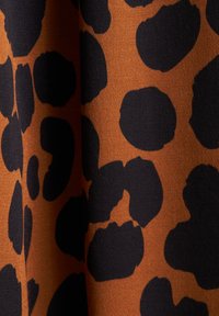 Tessuto leopardato con grandi macchie nere irregolari su uno sfondo arancione caldo. Texture liscia con una leggera lucentezza.