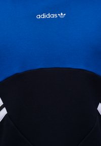 Μπλε και μαύρο ένδυμα Adidas με λευκό λογότυπο και τρεις λευκές ρίγες στις πλευρές.