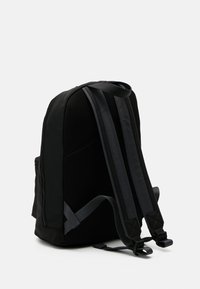 Zaino nero con dettagli in rete, spallacci regolabili e forma elegante e arrotondata. Presenta una tasca laterale e zip robuste.