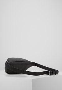Borsa a tracolla nera in pelle con finitura testurizzata, forma sottile, tracolla regolabile e accessori in argento. Chiusura a zip sulla parte superiore.