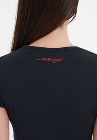 Black T-shirt with a close-fitting design, featuring a rounded neckline and red embroidered logo on the upper back.
