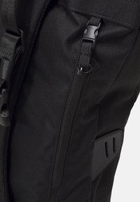 Sac à dos noir en nylon texturé, avec une poche latérale zippée, des bretelles ajustables et un panneau d'accent noir lisse.