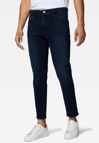 Mörkblå denimjeans med slim fit, fem fickor, subtil blekning och knappstängning, kombinerat med vita sneakers.