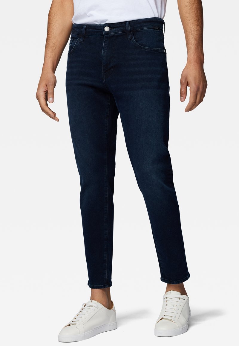 Mörkblå denimjeans med slim fit, fem fickor, subtil blekning och knappstängning, kombinerat med vita sneakers.