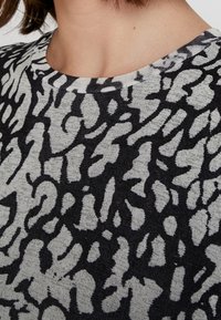 Svart och gråmönstrad stickad topp med rund halsringning; har abstrakta former och en strukturerad tyg. Närbild av designen.