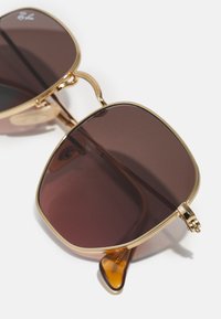 Occhiali da sole con montatura dorata e lenti di colore marrone. La montatura presenta un design elegante e dettagli testurizzati sulle tempie.