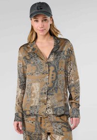 Shirt in bruin satijn met een paisleypatroon in blauw en wit, voorzien van een kraag en knoopsluiting, gedragen met bijpassende onderkleding.