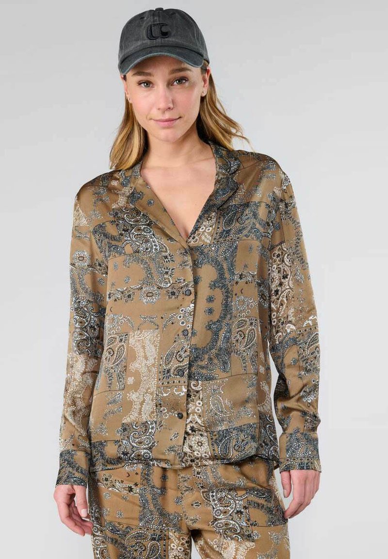 Shirt in bruin satijn met een paisleypatroon in blauw en wit, voorzien van een kraag en knoopsluiting, gedragen met bijpassende onderkleding.