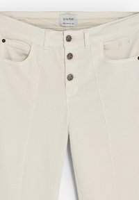 Pantalones de mezclilla color crema con corte recto, que cuentan con un cierre de cinco botones y dos bolsillos delanteros. Destacan acentos de calaveras en los botones.
