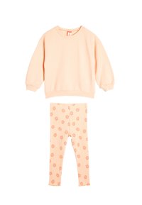 Sudadera melocotón con puños acanalados y cuello redondo, combinada con leggings acanalados que presentan un patrón floral en tonos melocotón a juego.