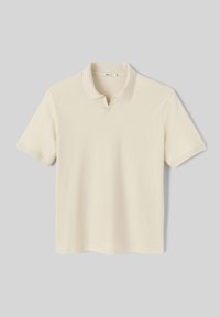 Polo à col crème en tissu tricoté texturé. Il présente un col classique et des manches courtes avec une subtile encochée en V.