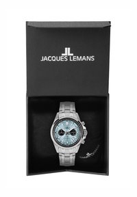 Sidabrinis nerūdijančio plieno laikrodis su šviesiai mėlynu ciferblatu, juodais subciferblatais ir poliruotu apyrankiu, pristatytas juodame dėkle su logotipu.