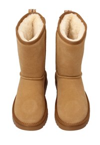 Zamszowe botki w kolorze orzecha włoskiego z miękką futrzaną wyściółką, zaokrąglonym noskiem i przeszyciami. Płaska gumowa podeszwa zapewnia komfort i stabilność.