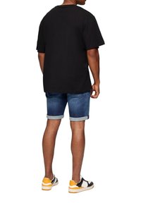 Maglietta nera a maniche corte, pantaloni corti di jeans con risvolti, e sneakers multicolori con accenti neri, bianchi e gialli.