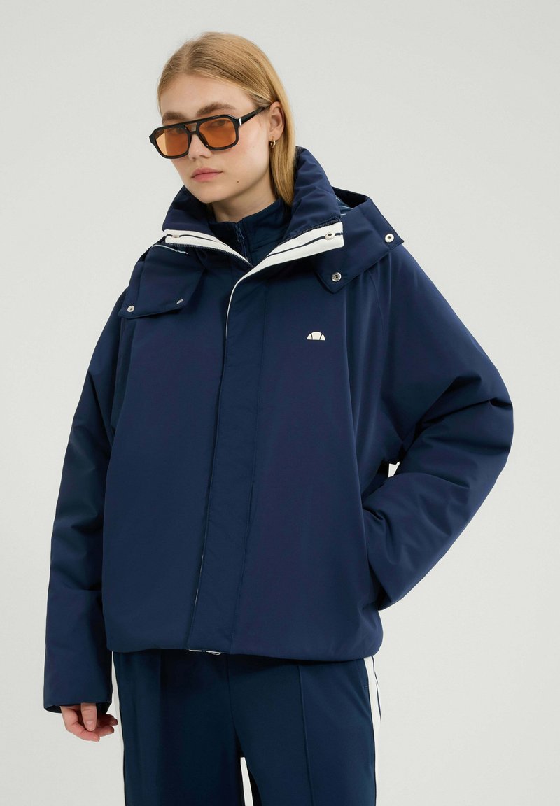 Granatowa zimowa kurtka z odpinanym kapturem, białymi akcentami i dwoma przednimi kieszeniami. Wykonana z gładkiego, wodoodpornego materiału.