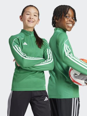Twee kinderen in groene sportjacks met witte strepen. De jacks hebben een hoge kraag en een gestructureerde stof. Eén houdt een voetbal vast.