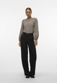 Top lungo a maniche con texture marrone chiaro e spalle imbottite, abbinato a pantaloni neri a gamba larga a vita alta e scarpe nere chunky.