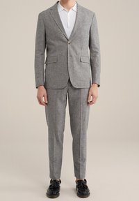 Grå texturerad kostym med en skräddarsydd kavaj med rektangulär krage och slim-fit byxor. Accessoarer inkluderar en vit polotröja och svarta skor.