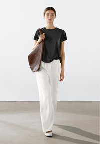 Sort kortærmet t-shirt, hvidt bredrandet bukser med lodrette striber og en vævet brun skuldertaske. Glat stof med en afslappet pasform.