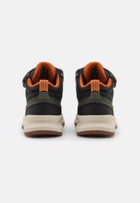 Chaussures de sport noires et olive avec des accents orange, dotées d'une tige texturée, d'un col rembourré et d'une semelle en caoutchouc contrastante.