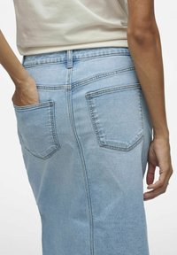 Gonna in denim azzurro chiaro con taglio dritto, dotata di due tasche posteriori e dettagli di cucitura in vista, indossata con una maglia di colore neutro.