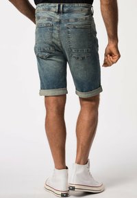 Pantalones cortos de mezclilla en azul claro con un acabado desgastado, puños enrollados y dos bolsillos traseros. Llevados con zapatillas altas blancas.