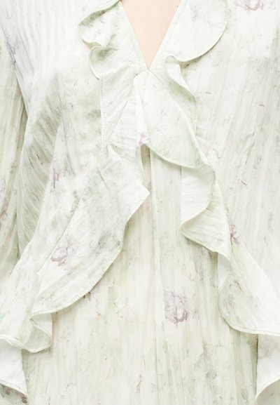 Ανοιχτοπράσινο υφασμάτινο μπλουζάκι με βολάν στον λαιμό, που διαθέτει λεπτό λουλουδάτο μοτίβο και απαλή υφή. Άνοιγμα με σχισμή στο μπροστινό μέρος.