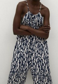 Navy and white patterned jumpsuit with thin straps, a pleated neckline, and wide legs, featuring a geometric design and lightweight fabric.
