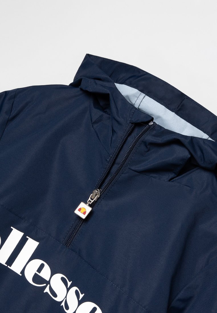 Chaqueta ligera de color azul marino con capucha, que presenta un cierre frontal de media cremallera, impresión de logo en blanco y una pequeña etiqueta de logo cerca de la cremallera.