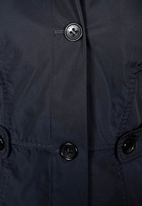 Marineblauwe jas met een gladde, glanzende textuur, voorzien van grote zwarte knopen en een dubbelzijdig ontwerp. Genaaide details langs de naden.